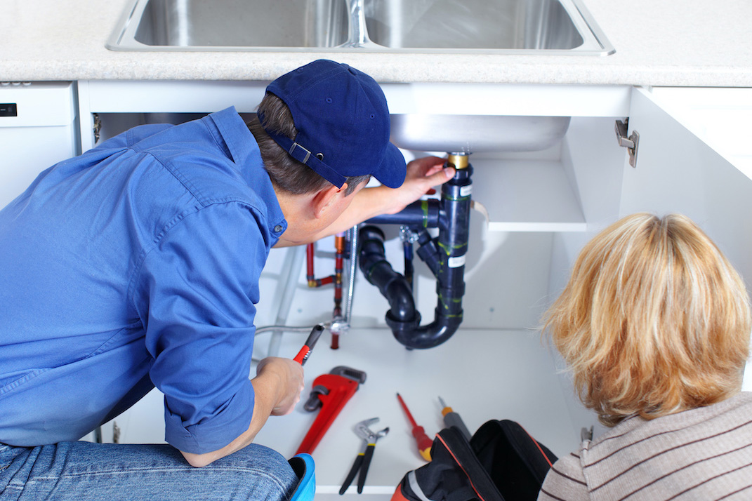Mature plumber fixing a sink at kitchen